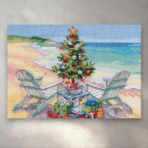 May include: Cross-stitch art showing a Christmas tree on a beach, decorated with ornaments and a starfish. Two white Adirondack chairs face the sea. Presents and a toy sailboat are at the tree's base. The scene is set against a blue sky and sandy beach.