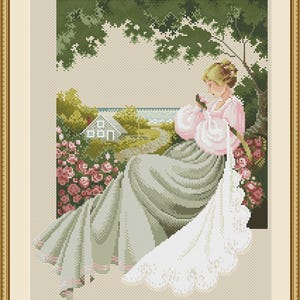 May include: Cross-stitch artwork of a woman in a pink and gray dress, holding a rose. The scene is set outdoors with a house, garden, and trees visible through a window. The artwork is framed in a gold-colored frame.