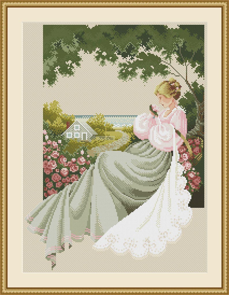 May include: Cross-stitch artwork of a woman in a pink and gray dress, holding a rose. The scene is set outdoors with a house, garden, and trees visible through a window. The artwork is framed in a gold-colored frame.