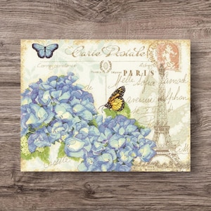 May include: A decorative canvas print featuring a blue hydrangea bouquet and two butterflies. The print has a vintage postcard design with the Eiffel Tower and text that reads "Carte Postale Paris".