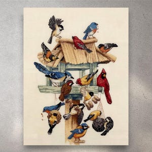 May include: A detailed needlepoint of a birdhouse filled with various colorful birds. The birds include blue jays, cardinals, and other species, perched on the birdhouse and surrounding structures. The artwork is set against a neutral background.