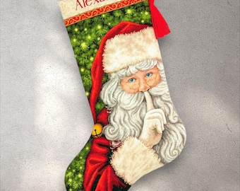May include: Christmas stocking with a Santa Claus design, finger to his lips, on a green and gold background. The stocking has a red tassel and the name "Alexander" printed at the top.
