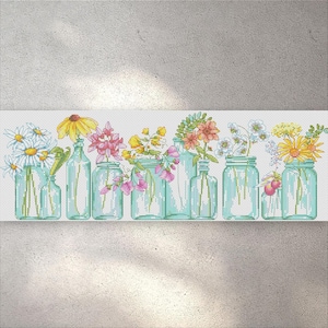 Puede incluir: Diseño de punto de cruz que presenta una fila de tarros de cristal llenos de flores coloridas. Los tarros varían en forma y tamaño, con un tinte azul claro. Las margaritas, los girasoles y otras flores añaden colores vibrantes al arreglo floral.