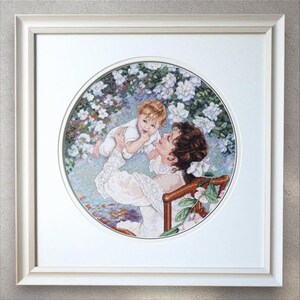 May include: Framed artwork featuring a mother and child in a garden setting. The artwork is a cross-stitch design, with the mother holding the child. The artwork is framed in a white frame.