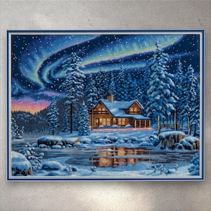 May include: Cross-stitch of a winter cabin scene under the aurora borealis. The cabin is nestled among snow-covered pine trees, with a lake reflecting the lights. The sky transitions from dark blue to purple and green.