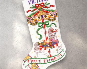 Könnte beinhalten: Weißer Weihnachtsstrumpf mit einem Karussellpferdmotiv. Der Strumpf trägt den lila Namen "Victoria", eine rot-grüne Schleife und die Worte "Merry Christmas". Das Karussellpferd ist grau und weiß mit bunten Akzenten.