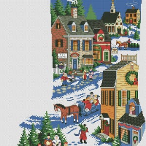 May include: A cross-stitch Christmas stocking featuring a winter village scene. The design includes houses, people, a horse-drawn sleigh, and the text "TOY SHOPPE" on a building. The color palette includes blue, red, green, and brown.