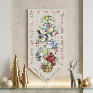 May include: A vertical cross-stitch wall hanging featuring a stylized Christmas tree in a basket with four colorful birds and a yellow star on top. The text "Friends Gather Together at Christmas" is stitched in red along the top and sides.