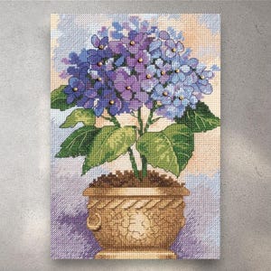 May include: Cross-stitch artwork of a hydrangea plant in a decorative pot. The flowers are a mix of purple and blue, with green leaves and a brown pot. The background is a light, textured pattern.