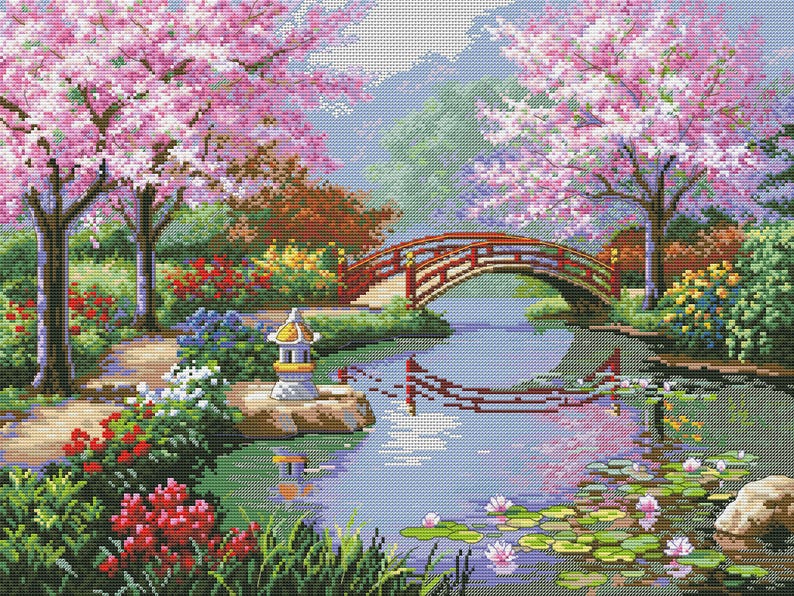 May include: A cross-stitch landscape depicts a serene Japanese garden scene. A red arched bridge spans a river, with cherry blossom trees in full bloom. The scene includes a stone lantern, water lilies, and lush greenery.