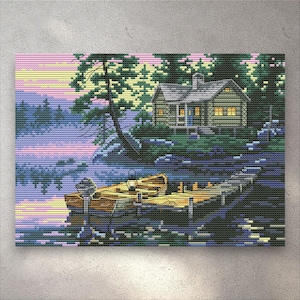 Puede incluir: Un patrón de punto de cruz que representa una cabaña junto al lago al atardecer. La escena muestra un pequeño bote de madera amarrado a un muelle, rodeado de árboles de color verde oscuro y un cielo rosa y amarillo reflejado en el agua.