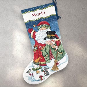 May include: Christmas stocking with a blue top and a white base. The stocking features a Santa Claus and snowman design, with the name "Marla" embroidered at the top. The design includes a red Santa suit, a green coat, and a snowman with a black hat.