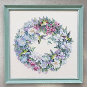 Könnte beinhalten: Gerahmtes Kreuzstich-Kunstwerk mit einem Kranz aus Blumen in Blau-, Lila-, Rosa- und Weißtönen. Mehrere grüne und rote Kolibris sind um den Blumenkranz herum abgebildet. Der Rahmen ist helltürkis.