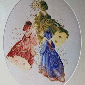 May include: A framed cross-stitch artwork featuring three figures in ornate gowns. The figures are in shades of red, green, and blue, with intricate details and sparkling accents. The artwork is set against a white background.