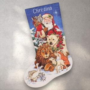 May include: Christmas stocking with a blue top and a white bottom. The stocking features Santa Claus, a polar bear, a lion, a fox, a lamb, and geese. The name "Christina" is printed on the top.