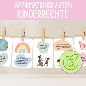 Może przedstawiać: Zestaw kart afirmacyjnych dla dzieci, z akwarelowymi ilustracjami i tekstem. Karty są przypięte do sznurka drewnianymi spinaczami. Karty mają obrazy globu, tęczy i motyla, ze słowem "Eco Friendly".