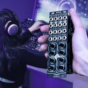 May include: A black 4VCA audio module with multiple input and output jacks, knobs, and the text "TEMBRA KAXIMIA". The module is held in a hand, with a person wearing headphones and using a computer in the background. The scene is lit with purple hues.