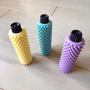 May include: Three decorative bottle stoppers in pastel shades. A yellow, a teal, and a purple stopper, each with a black top and a textured, cone-shaped body. They are displayed on a light wooden surface.