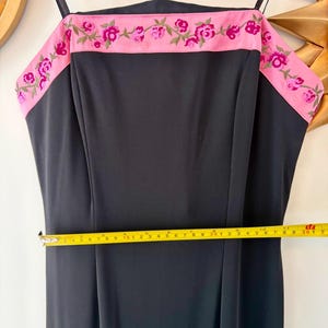 Puede incluir: Vestido negro con ribete rosa bordado con flores. El vestido tiene tirantes finos y un corpi&ntilde;o ajustado. La cintura mide aproximadamente 40 cm de ancho. El ribete presenta flores rosas y hojas verdes.