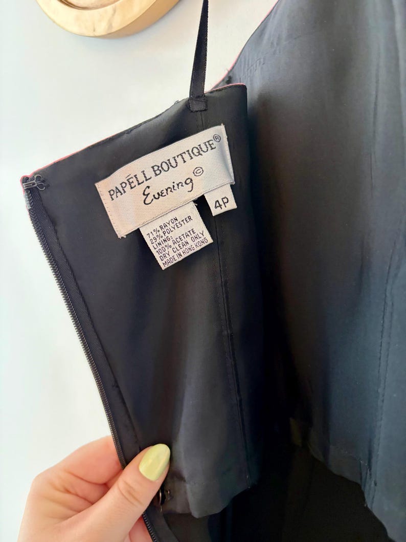 Puede incluir: Primer plano de un vestido de noche negro con cremallera y una etiqueta que dice "PAPELL BOUTIQUE Evening". La etiqueta tambi&eacute;n indica que el vestido es talla 4P y est&aacute; hecho de ray&oacute;n, poli&eacute;ster y acetato. El vestido est&aacute; hecho en Hong Kong.