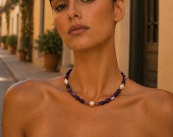 May include: A necklace featuring a repeating pattern of smooth, oval-shaped deep purple amethyst beads and round white pearls. The design includes small gold-toned spacers between the beads, with a central white pearl flanked by two small purple accents.