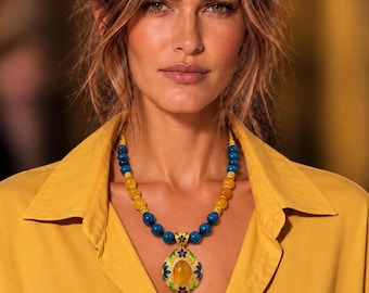 May include: A necklace featuring alternating blue and yellow spherical beads with a central oval pendant. The pendant has a yellow stone center surrounded by green leaf motifs and small blue and red flower accents on a gold-toned metal base.