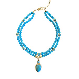 May include: A double-strand necklace featuring round turquoise beads interspersed with small gold-toned metal spacers. The necklace includes a central teardrop-shaped turquoise pendant suspended from a gold-toned metal bail and a gold-toned chain clasp.