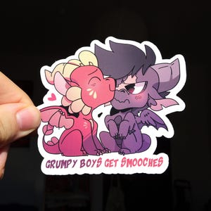May include: A sticker with a cartoon illustration of two dragons, one pink and one purple, kissing. The pink dragon has a kiss mark. The text "GRUMPY BOYS GET SMOOCHES" is written across the bottom.