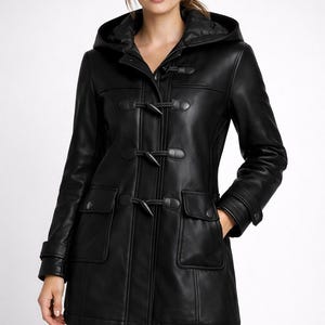 Puede incluir: Abrigo negro de cuero con capucha, cierres de palanca y dos bolsillos delanteros. El abrigo presenta un diseño clásico de abrigo duffle con un corte entallado. La capucha está forrada con una tela en contraste. Prenda exterior versátil.