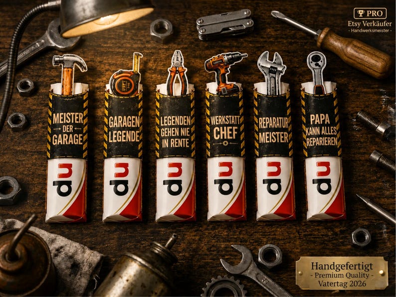 K&ouml;nnte beinhalten: Sechs dekorative Geschenke zum Thema Werkzeug mit deutschem Text, darunter "Meister der Garage" und "Werkstatt Chef". Jedes hat ein Miniaturwerkzeug oben, wie einen Hammer oder Schraubenschl&uuml;ssel, und ein rot-wei&szlig;-schwarzes Design. Der Hintergrund enth&auml;lt Werkzeuge.