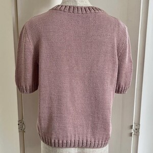 Może przedstawiać: Sweter w kolorze malwy, z kr&oacute;tkimi rękawami i okrągłym dekoltem.