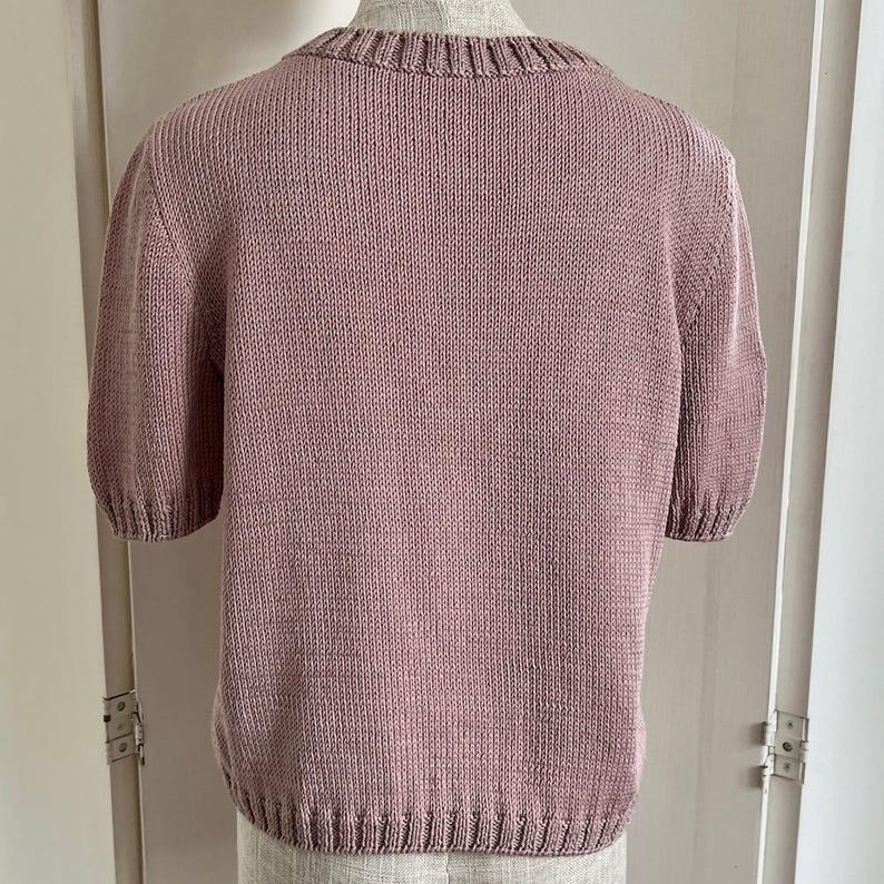 Może przedstawiać: Sweter w kolorze malwy, z kr&oacute;tkimi rękawami i okrągłym dekoltem.