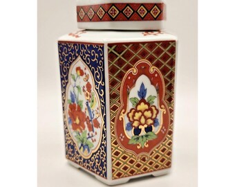 Peut inclure: Un pot en céramique hexagonal blanc avec un couvercle assorti. Le pot est décoré de motifs floraux et géométriques rouges, bleus et dorés. Le couvercle présente un motif de losanges répétés en rouge et or. Un récipient de stockage décoratif.