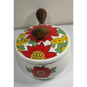 Może przedstawiać: Biała ceramiczna cukiernica z drewnianym uchwytem i pokrywką. Pokrywka i miska zdobione są czerwonymi i żółtymi wzorami kwiatowymi. Uchwyt i gałka pokrywki wykonane są z ciemnego drewna.