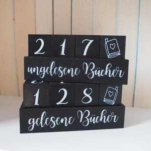 Könnte beinhalten: Schwarze Holzblöcke mit weißen Zahlen und Text. Die Blöcke schreiben "217" und "128" mit einem Buchsymbol. Der Text auf den Blöcken lautet "ungelesene Bücher" und "gelesene Bücher".