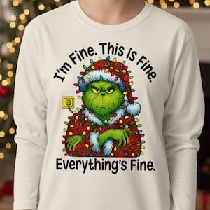 May include: A long-sleeved, off-white shirt featuring a cartoon Grinch character wearing a Santa hat and Christmas lights. The text "I'm Fine. This is Fine. Everything's Fine" is printed around the Grinch.