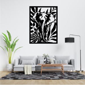 Peut inclure: Décor mural d'éléphant noir et blanc. L'œuvre présente une silhouette détaillée d'un éléphant entouré de feuilles tropicales. La pièce est encadrée dans un cadre noir et convient à la décoration intérieure.