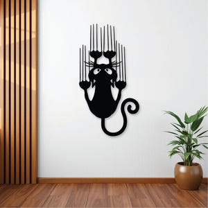 May include: Black silhouette of a cat with its claws extended, hanging upside down from a wall. The cat has a surprised expression on its face.