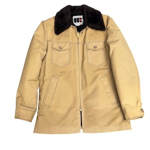 May include: Tan jacket with a brown faux fur collar, a zipper closure, and two chest pockets. The jacket has two side pockets and buttoned cuffs. The stitching is a darker brown color. The jacket has the letters "UB" on a tag.