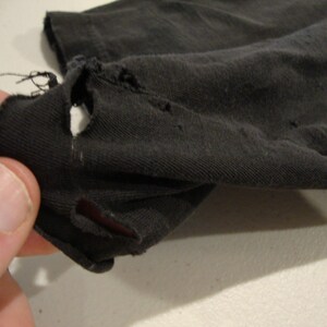 May include: Close-up of a black fabric with a hole in it. The fabric is worn and has a rough texture.