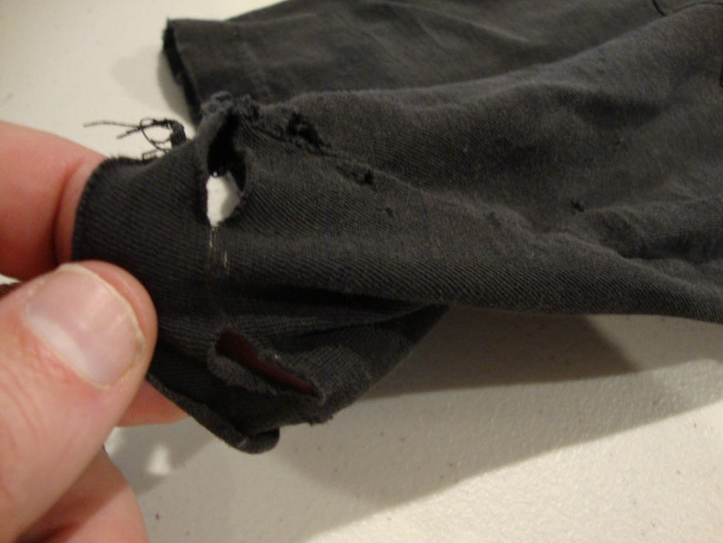 May include: Close-up of a black fabric with a hole in it. The fabric is worn and has a rough texture.
