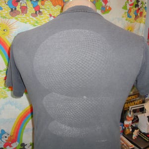 Op de afbeelding: Een grijs T-shirt met een witte afbeelding van een Mickey Mouse-hoofd op de rug. De afbeelding is een zeefdruk met een gaaspatroon.