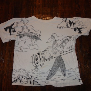 May include: White t-shirt with a black and white graphic print of a hummingbird, a clock, and birds flying in the sky.