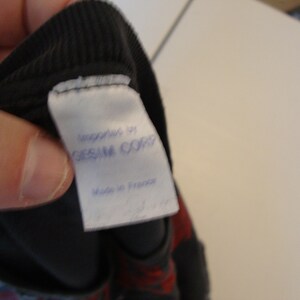 May include: A white tag sewn into a black garment with the text "Manufactured by GESSAM CORP" and "Made in France" printed in blue ink.