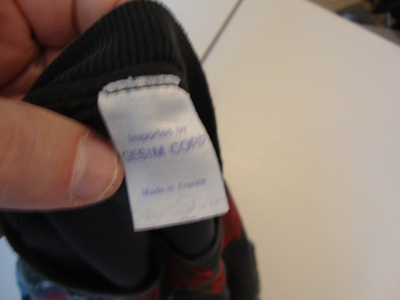 May include: A white tag sewn into a black garment with the text "Manufactured by GESSAM CORP" and "Made in France" printed in blue ink.