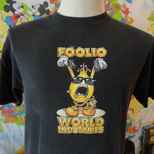 May include: Black t-shirt with a yellow cartoon character holding guns and wearing sunglasses. The character is labeled "Foolio" and "World Industries".