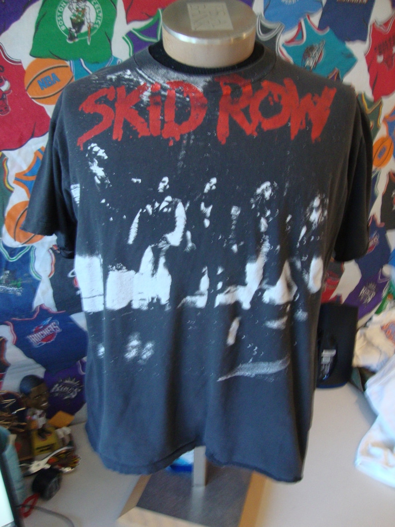 May include: Black t-shirt with a white and gray image of the band Skid Row. The band's name is printed in red letters across the top of the shirt.