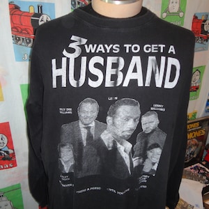 May include: Black long-sleeved t-shirt with a white graphic that reads "3 Ways to Get a Husband". The graphic features three men's faces:  Bully Dee Williams, Leon, and Lenny Williams. The text "Never Know a Person Until You're Together" is printed below the graphic.