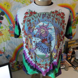 May include: Tie-dye t-shirt with a colorful graphic of a jester with a skull face and the word "GRATEFUL" in a psychedelic font.