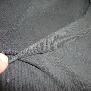 Puede incluir: Primer plano del cuello de una camiseta negra que muestra la tela de punto de canal&eacute;.